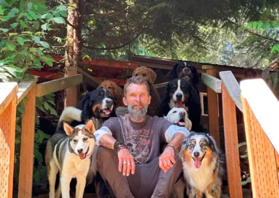 Camp counselor sitting on wooden steps surrounded by a pack of happy dogs at Camp Happy Paws
